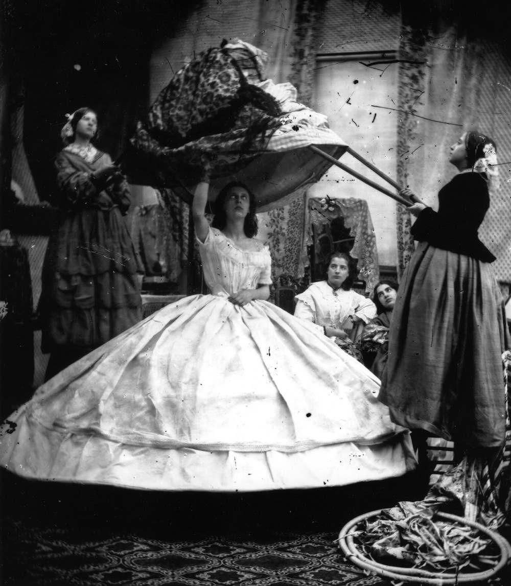 dressing with the assistance of several maids who require long poles to lift her dress over her head and other ingenious means of navigating her enormous hoopskirt.