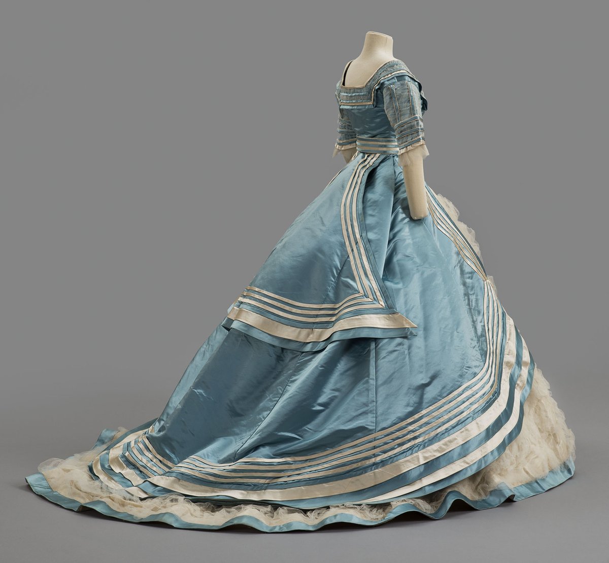 By 1868, the fullness of women's skirts had moved to the back, and a bustle was needed to support fashionable puffed overskirts and large sashes. The high back interest continued in the early 1870s as the bustle gradually swelled in size.
