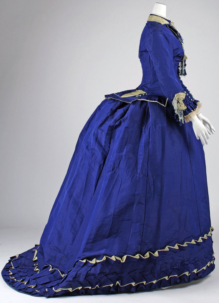 The transition from the voluminous crinoline-enhanced skirts of the 1850s and 1860s can be seen in the loops and gathers of fabric and trimmings worn during this period.