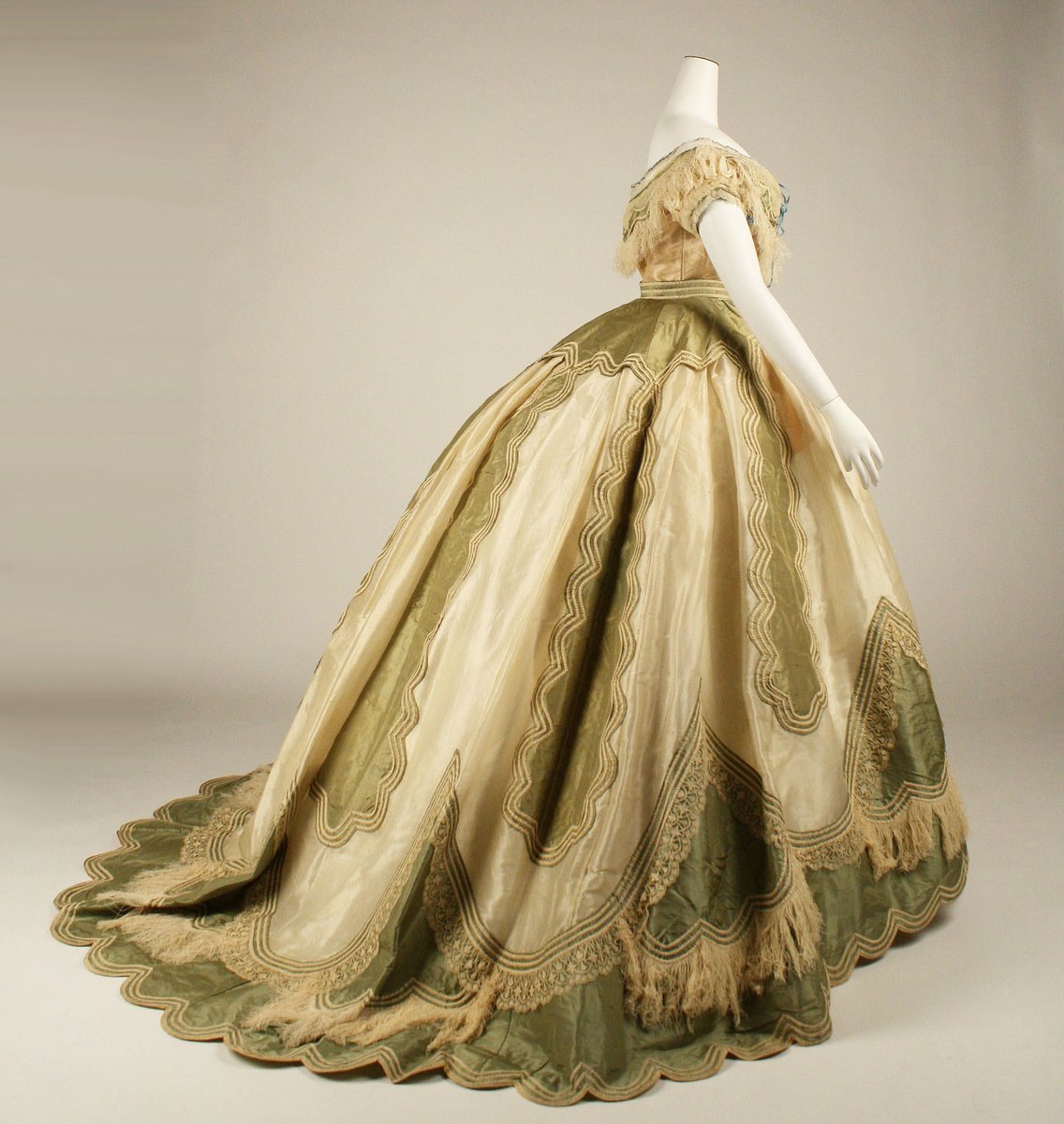 The transition from the voluminous crinoline-enhanced skirts of the 1850s and 1860s can be seen in the loops and gathers of fabric and trimmings worn during this period.