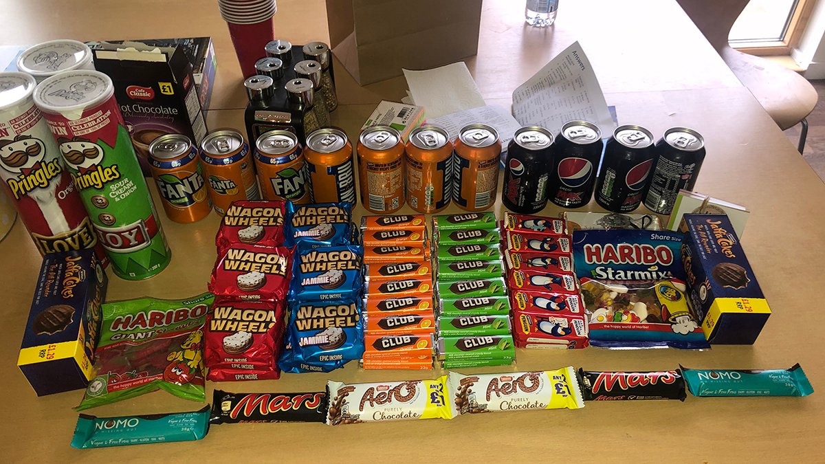 a photo of table top of biscuits, crisps, cans of drinks, sweets and chocolate.