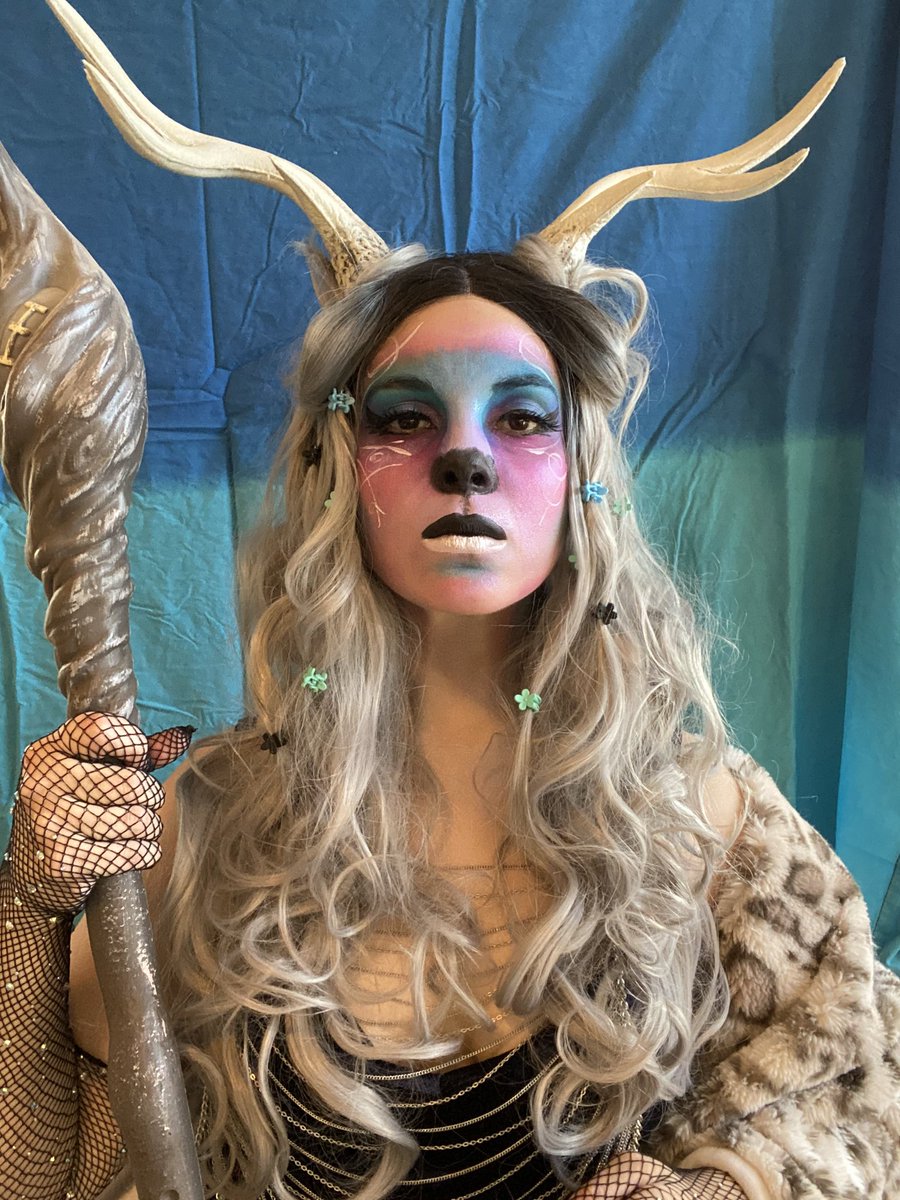 Kristy wearing antlers, a wig, and a lot of sparkly pink and blue faun makeup while holding a gnarled staff.