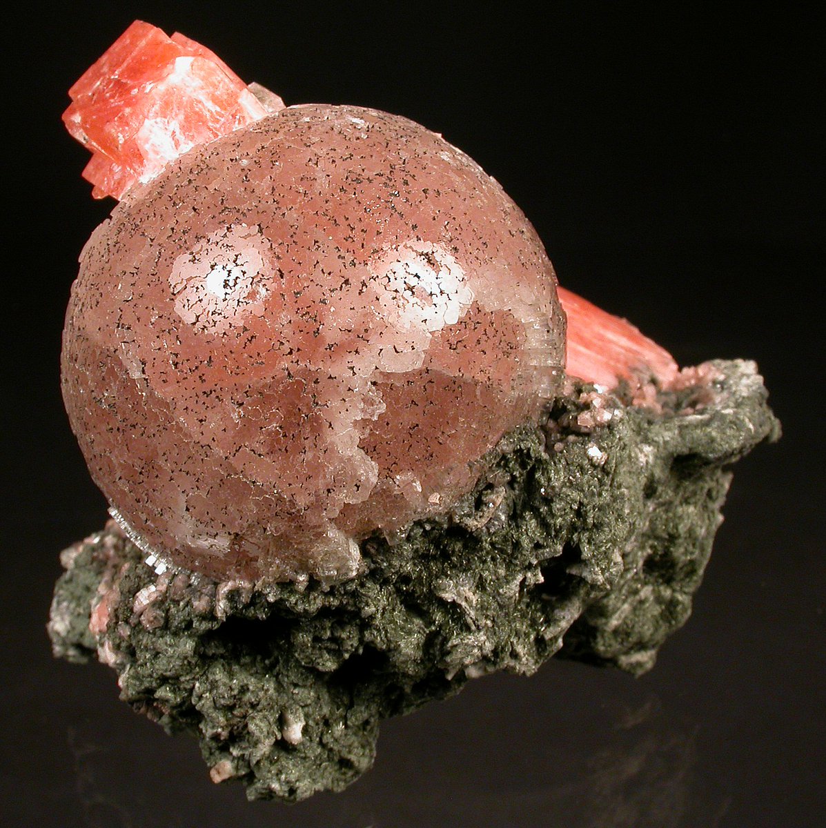 Round pale pink ball of leifite-eirikite with green amphibole and columnar pink-orange serandite behind it.