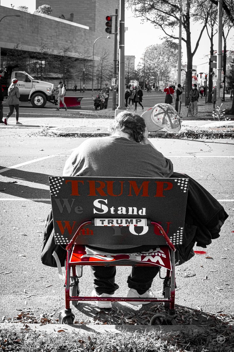 My absolute favourite shot of the series; a man sits on a sign reading "TRUMP We Stand With YOU".In his lap are copies of  @RyuhoOkawa's book with giant stickers reading "GOD CHOSE TRUMP".