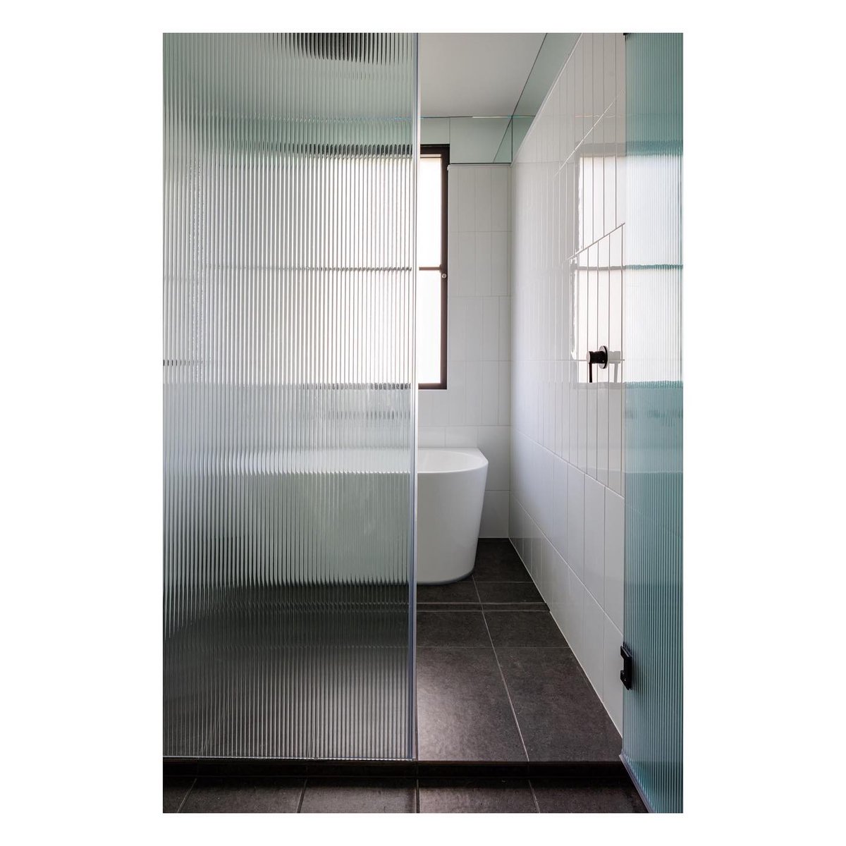 The combined shower and bath area behind the ribbed glass provides a sense of privacy and spaciousness. #tileinsert #drainage #shower #bathroomdesign