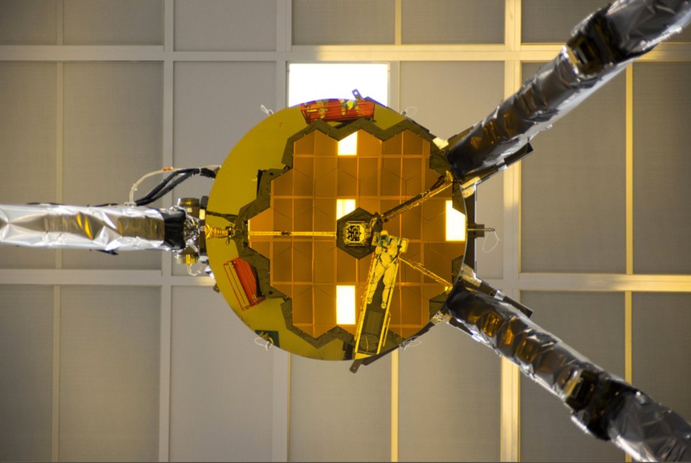 Reflected within the small, circular secondary mirror of the James Webb Space Telescope is the telescope's primary mirror, as well as optical engineer Larkin Carey. Carey is dressed in a cleanroom suit and holding a camera to his face. Credit: Ball Aerospace