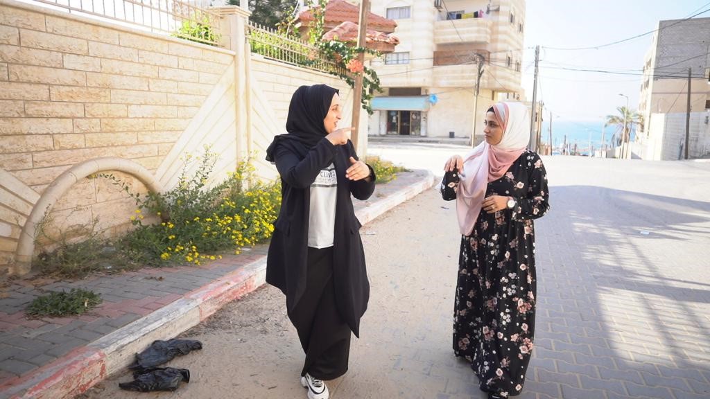 Two women with hearing disabilities communicate using sign language while walking down a street. 