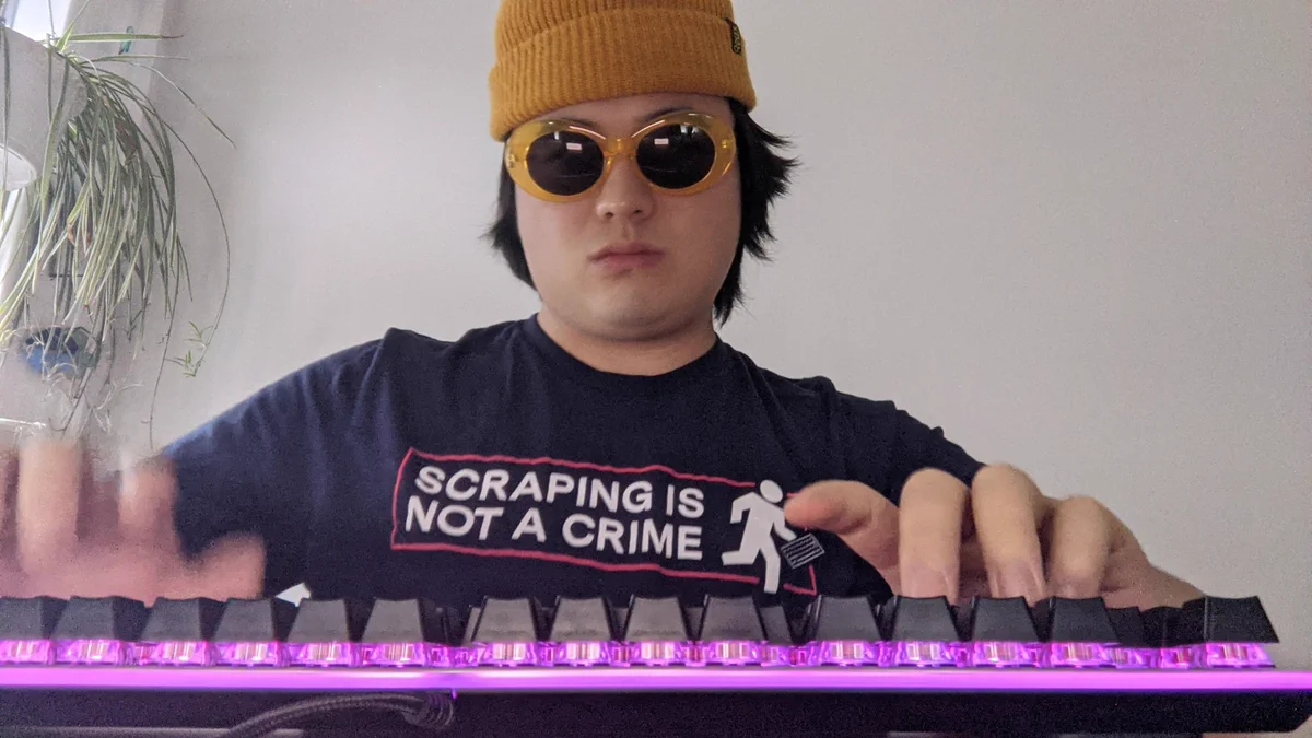 Man typing on keyboard with sunglasses and "scraping is not a crime" t-shirt.