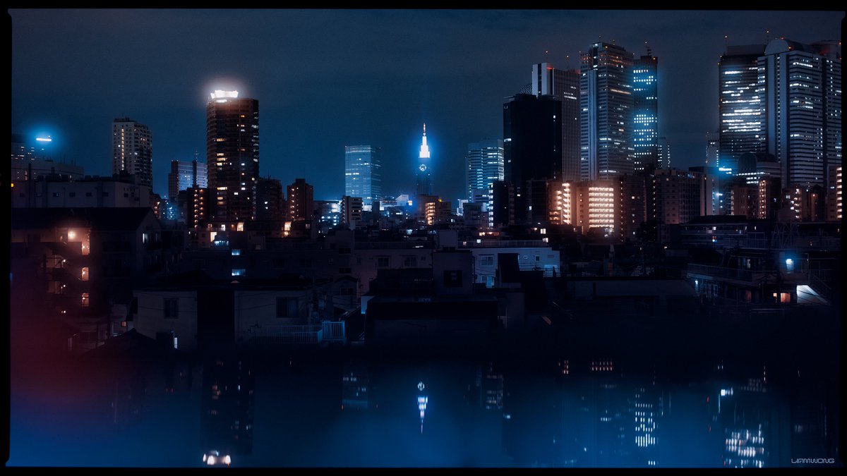 Photography by Liam Wong of Tokyo at night. A cityscape shot of Shinjuku, Tokyo. It is blue in color with warm colored lights. Maybe modern buildings can be seen. At the center of the image is the Docomo Tower with a clock on it. The image has a reflected view of the city on the lower half.