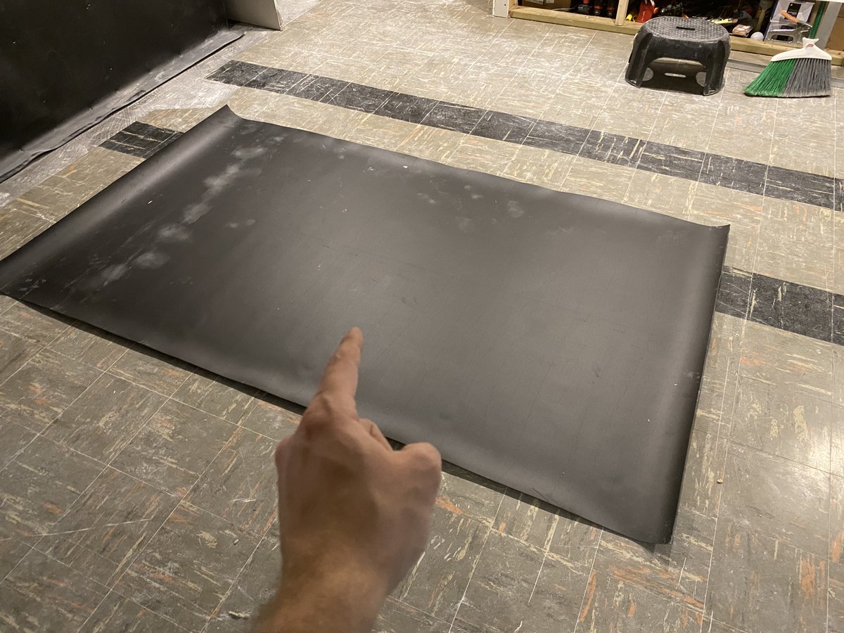 Hand pointing at 4 foot by 7 foot sheet of mass loaded vinyl laying on the floor