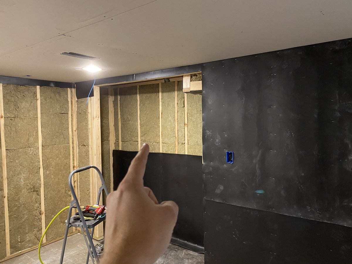 Hand pointing at a future closet wall, with a 4 foot by 7 foot gap awaiting the mass loaded vinyl 