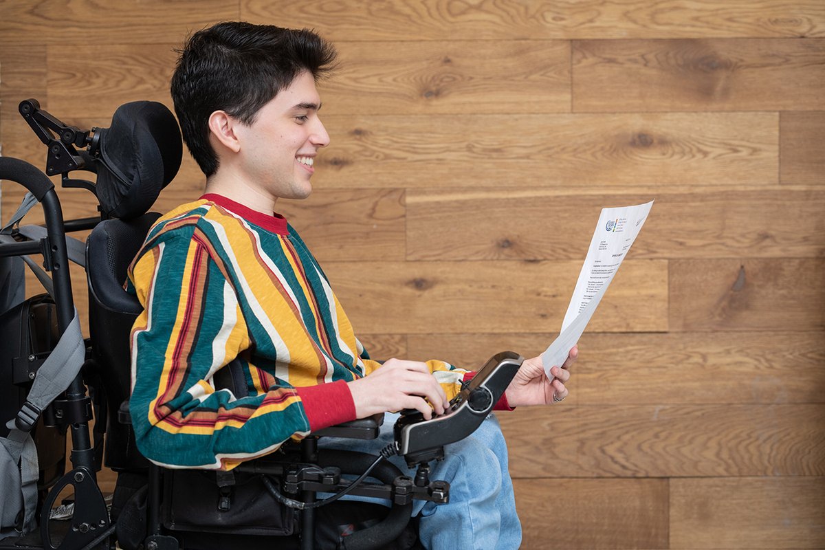 Student in a wheelchair reading a paper from the college.