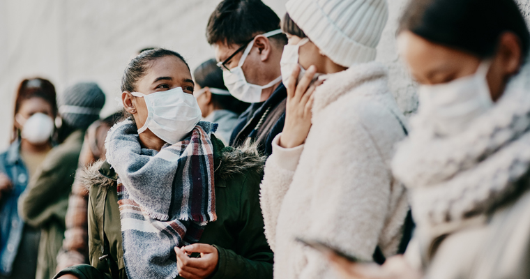 People stand around wearing masks in a city setting.