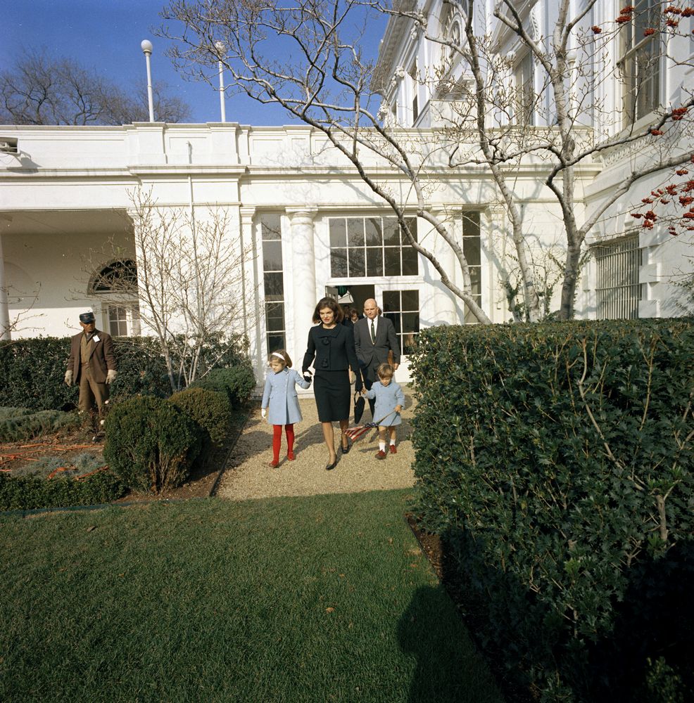 After her husband's murder, Jacqueline Kennedy and John and Caroline depart White  House through Rose Garden she created, today 1963. (Dave Powers in rear.)  She ensured that when they left, her children, image size:986x1000