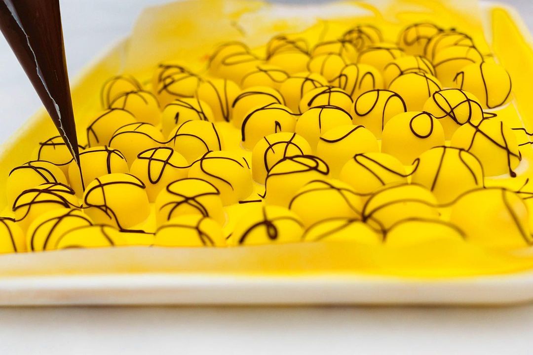 Yellow chocolates by Studio Chocolate being decorated with a dark brown syrup.