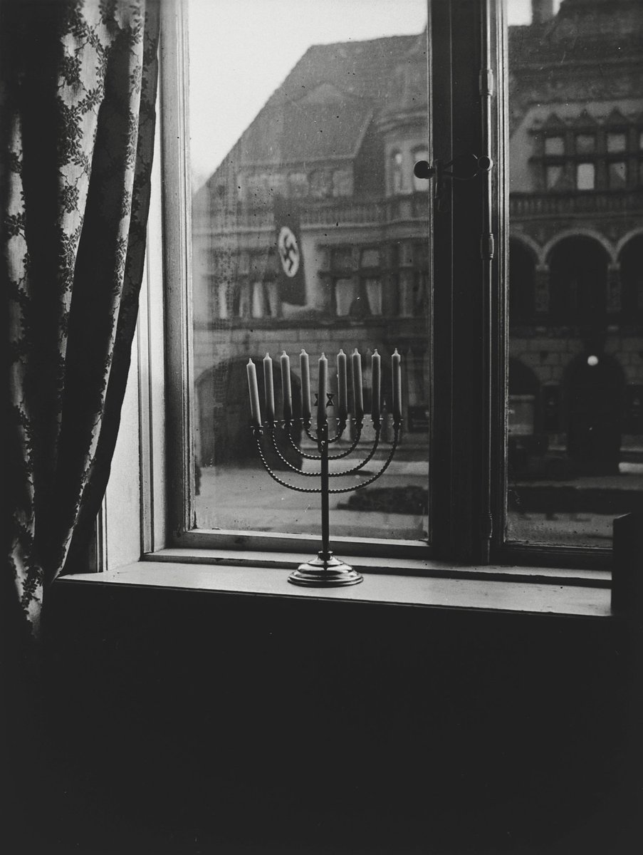 Dieses Foto wurde 1932 in Kiel von Rachel Posner, Frau eines Rabbiners, aufgenommen. Auf die Rückseite des Fotos schrieb sie: 'Chanukkah 5692 (1932) 'Juda verrecke' Die Fahne spricht – 'Juda lebt ewig' Erwidert das Licht.' Möge das Licht immer stärker sein als die Dunkelheit!
