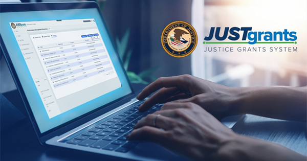 Photo of hands typing on a laptop with JustGrants website on screen.