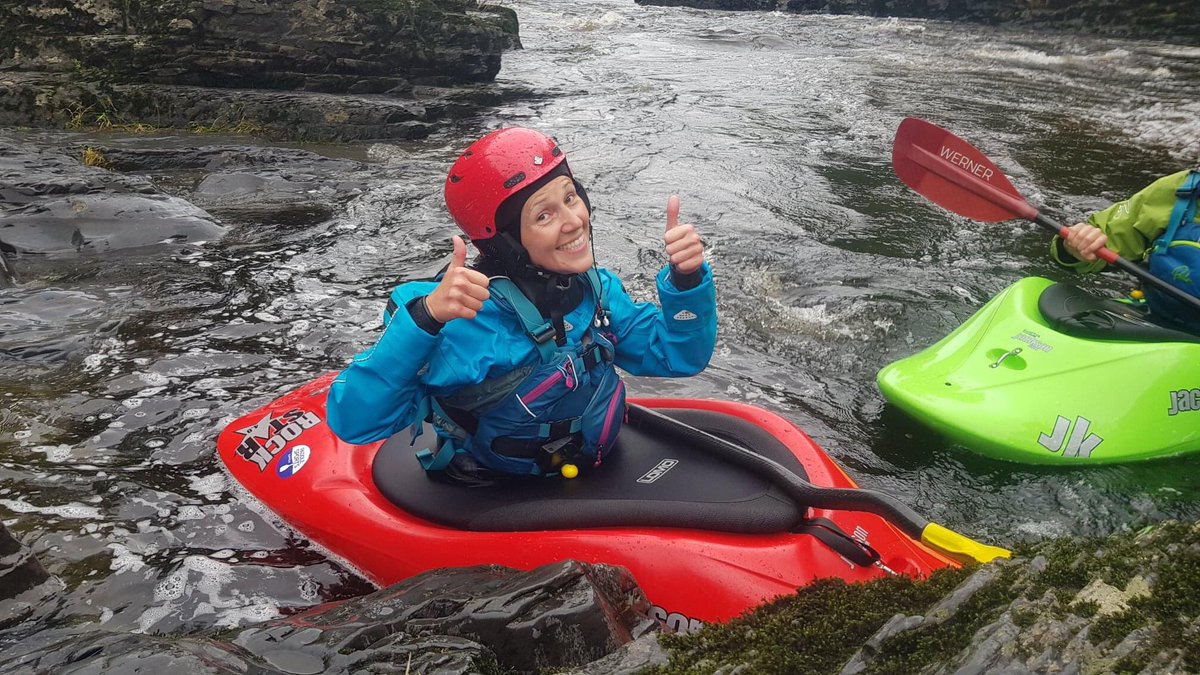 Lisa in a kayak with a big smile and her thumbs up after running a white water feature for the first time