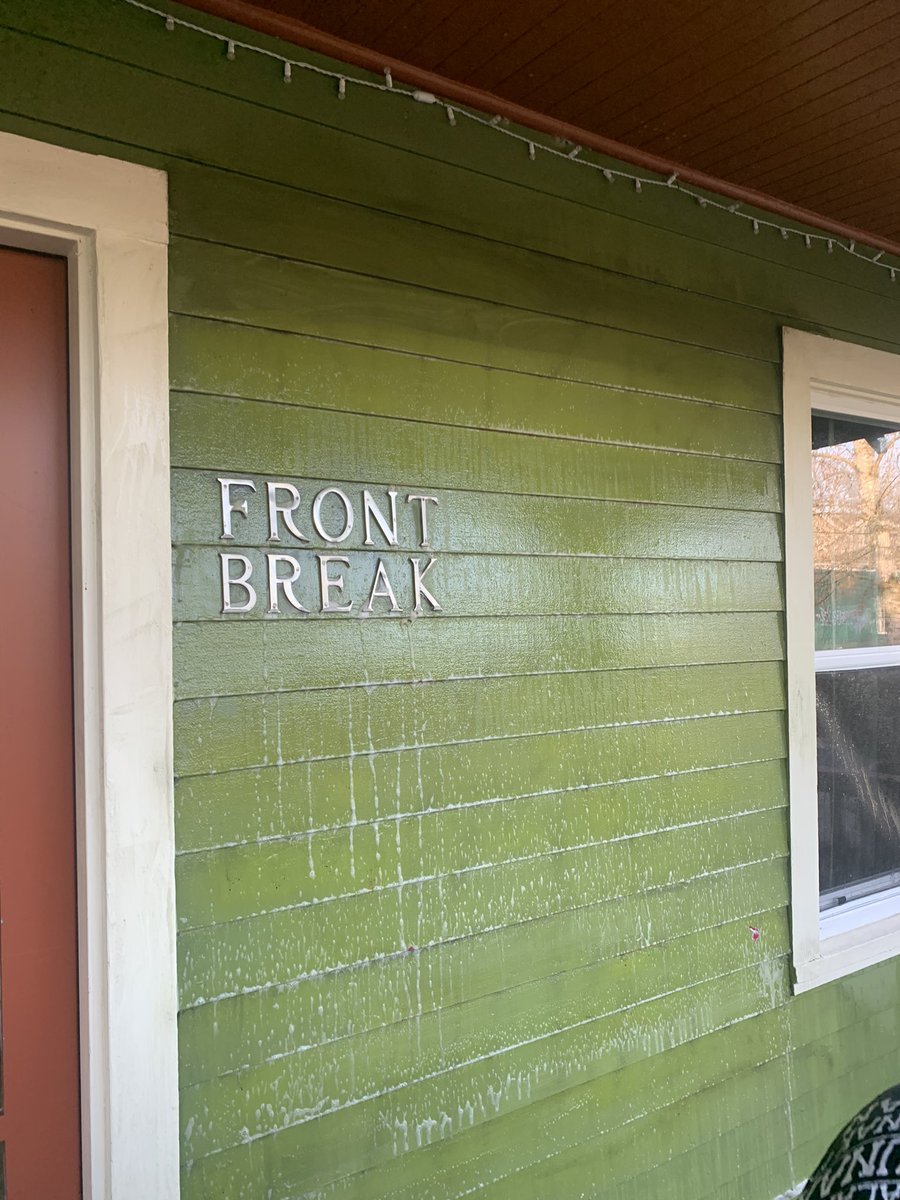 a green wall that has been recently scrubbed of graffiti. only very faint black lines remain. brass letters on the side of the building read “front break”
