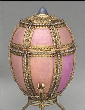 There is an emerald at each intersection of the lines separating the panels, and the egg is crowned with a medallion of radiating leaves around a cabochon star sapphire. The opposite end of the egg is chased with additional acanthus leaves.