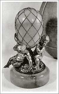 The egg is hinged, and a large diamond sits at its base. Originally it was supported on a base of three silver putti said to represent the three sons of the imperial couple, the Grand Dukes Nicholas, George and Michael.The putti were set on a jadeite base, now lost.