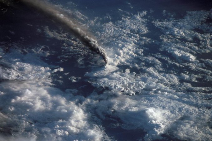 Aerial photo of a volcano erupting, surrounded by clouds.