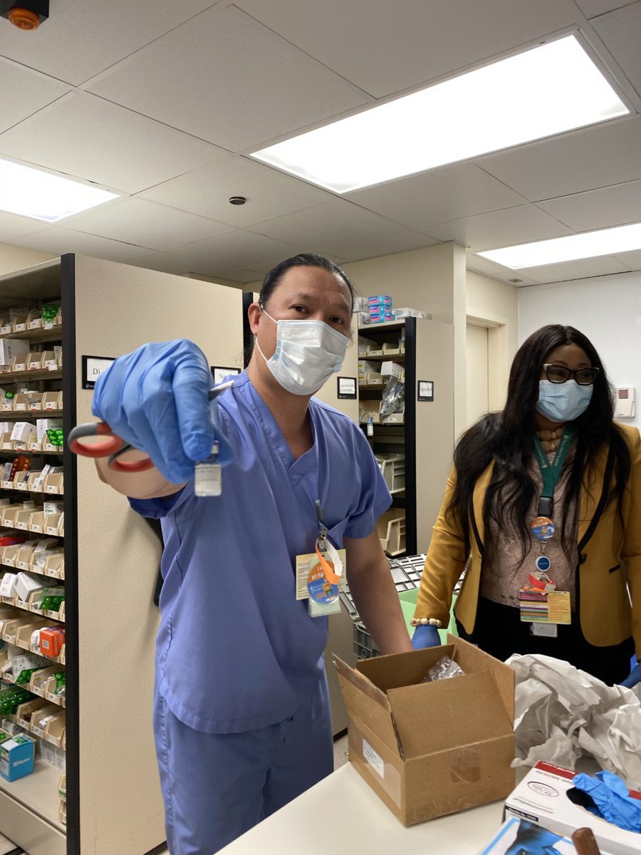 A hospital worker wearing blue scrubs holds a dose of the COVID-19 vaccine in a gloved hand.