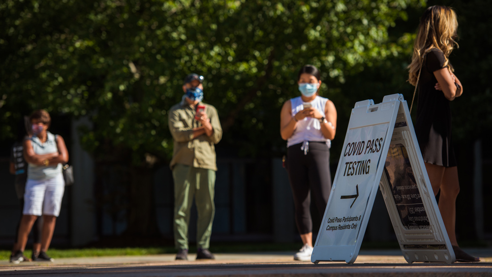 People standing physically distanced in a line waiting to get a Covid-19 test on a warm day.