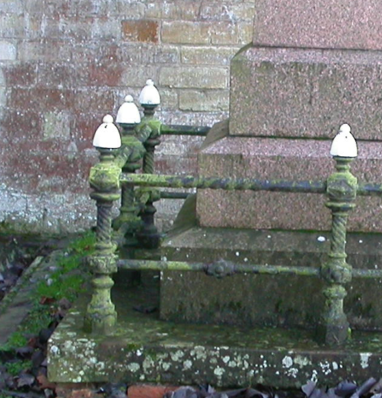 On the church wall behind the railings there is a brown block of ironstone in a predominantly limestone wall. Much of this shaded wall has a reddish crust of Trentepohlia alga (not a lichen).