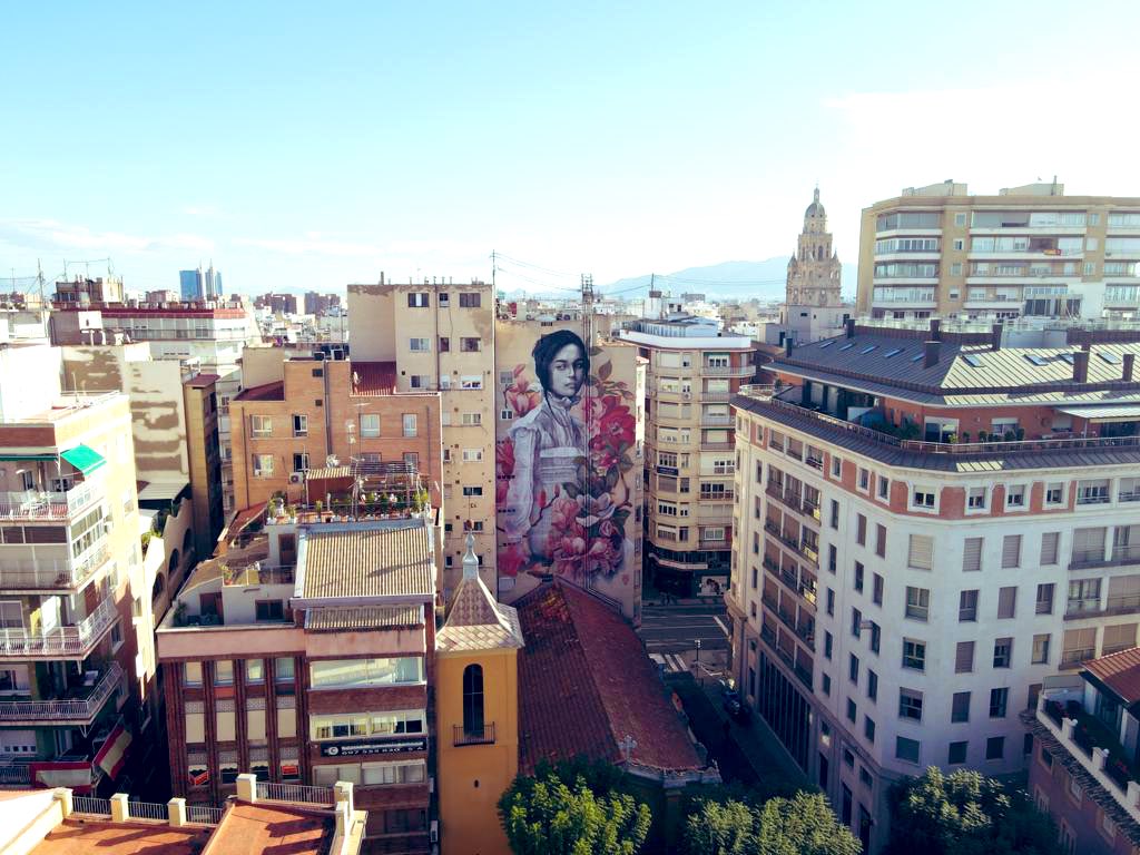 Desde hoy, esta murciana envuelta en flores contempla uno de los entornos históricos más bonitos de nuestra ciudad. 

Esta intervención urbana es obra de la muralista <a href="/lulagoce/">Lula Goce</a> , que continúa así conquistando al mundo.

🌺🌸🌺
