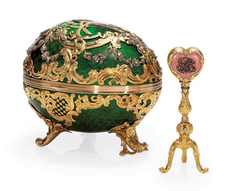In this egg, the surprise is a gold tripod surmounted by a translucent enameled rose-colored engraved heart with the initials "B.K." (Barbara Kelch) set with diamonds on one side and the year, "1902" also set with diamonds on the other.