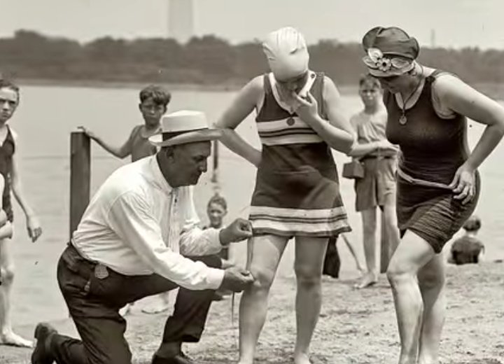 POLICEMAN MEASURING A WOMAN'S BATHING SUIT TO CHECK IF IT MEETS MINIMUM LEGAL LENGTH, 1920S.