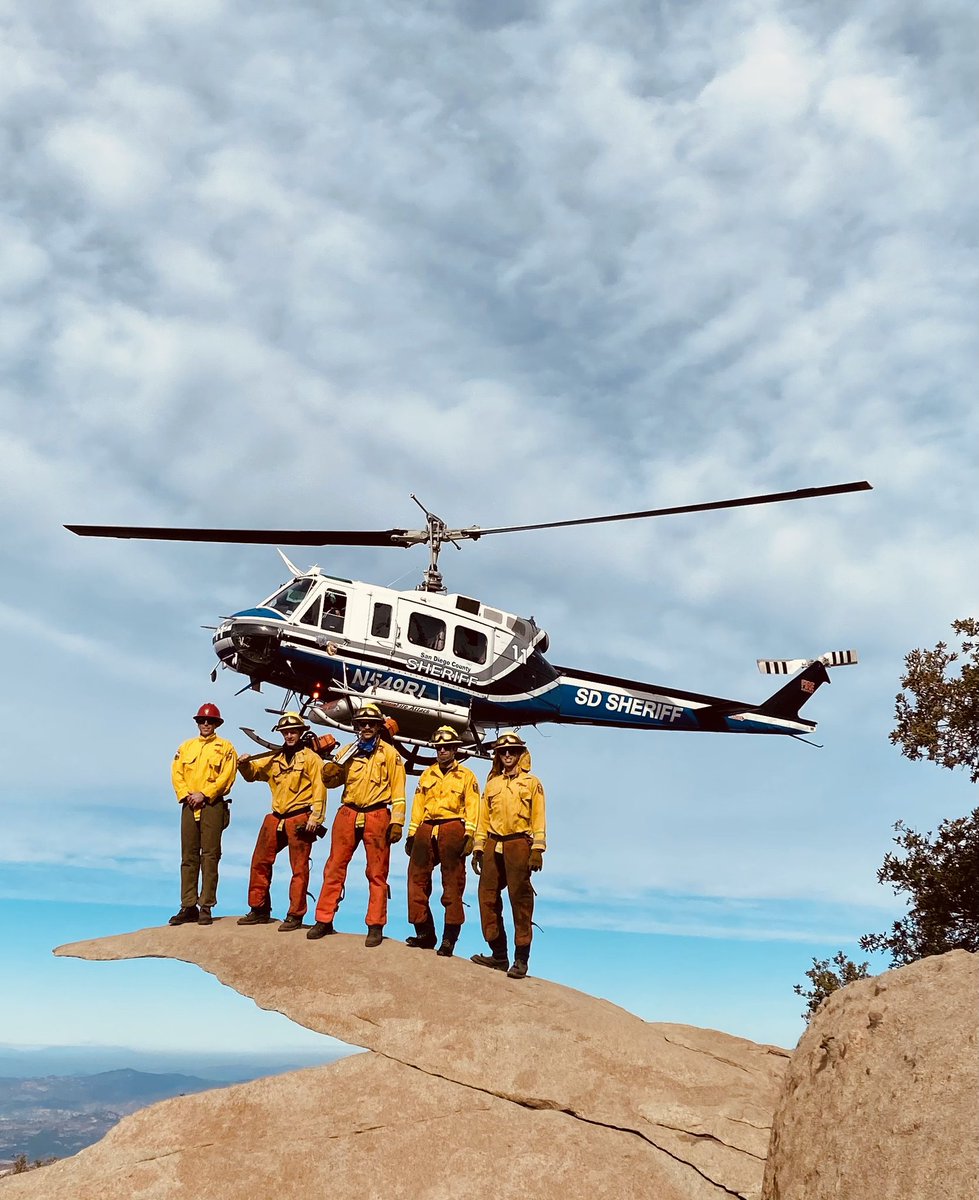 Sheriff’s Department helicopter hovering in the clouds with CAL FIRE firefighters standing on potato chip rock on Mt. Woodson summit in Ramona.