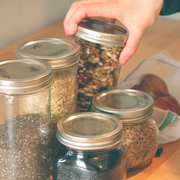 A hand reaches for glass jars filled with dry beans and grains.
