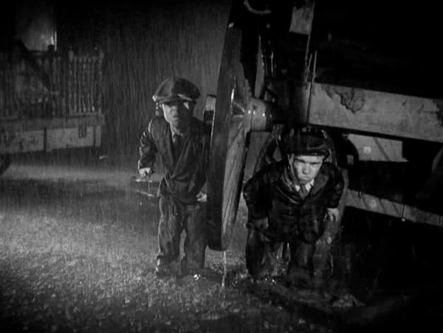 Two characters in Tod Browning's Freaks standing by a wooden cart in the pouring rain, cinema in the rain