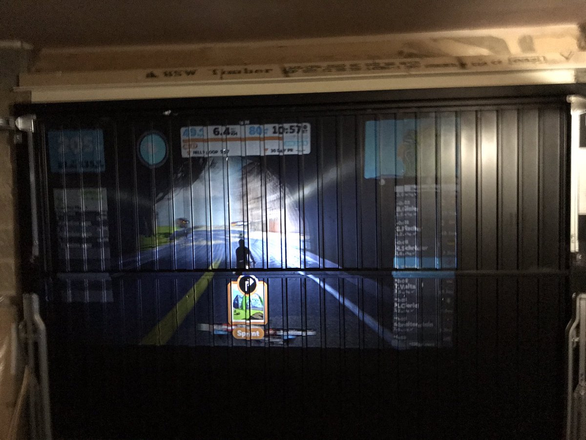 Petethacker's tweet image. Current experimental Zwift garage set up. Might invest in a proper projector screen rather than the garage door!