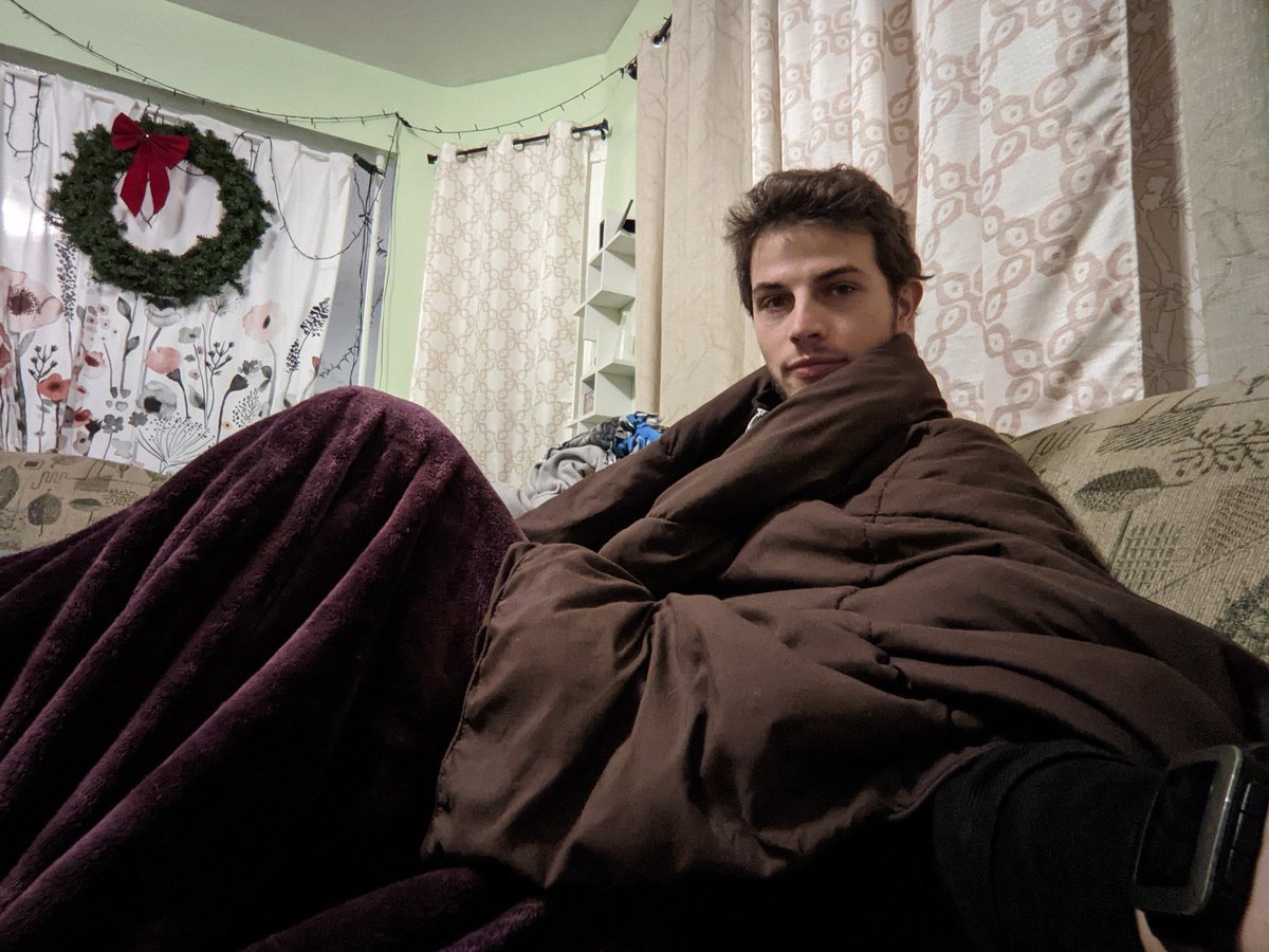 Ian sitting on his couch, wrapped in a blanket and comforter.