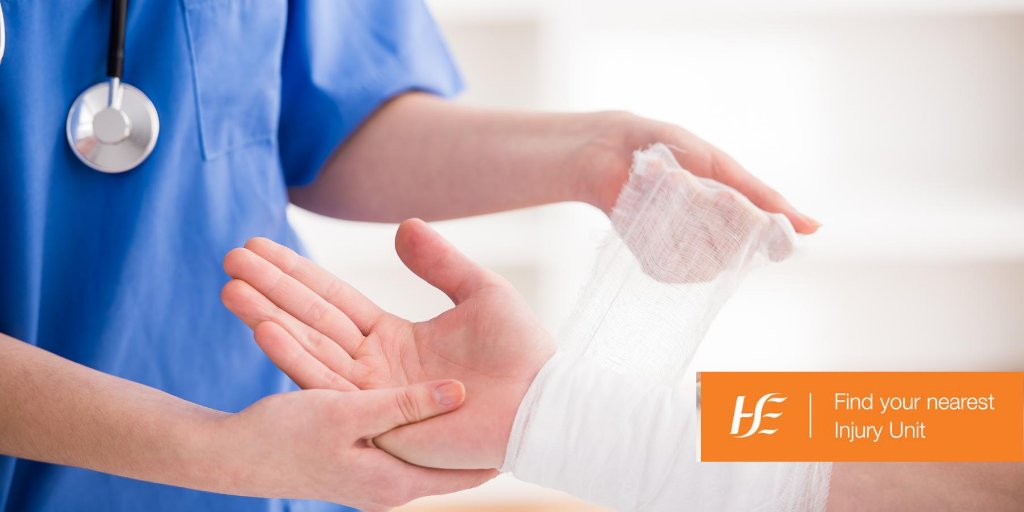 A nurse in blue scrubs wraps an injured arm in white gauze.