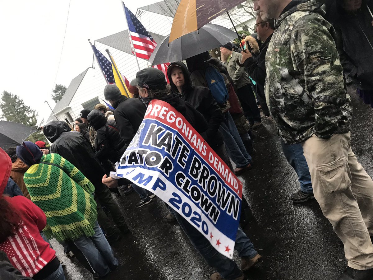 Man hold signs reading “Kate Brown dictator clown”