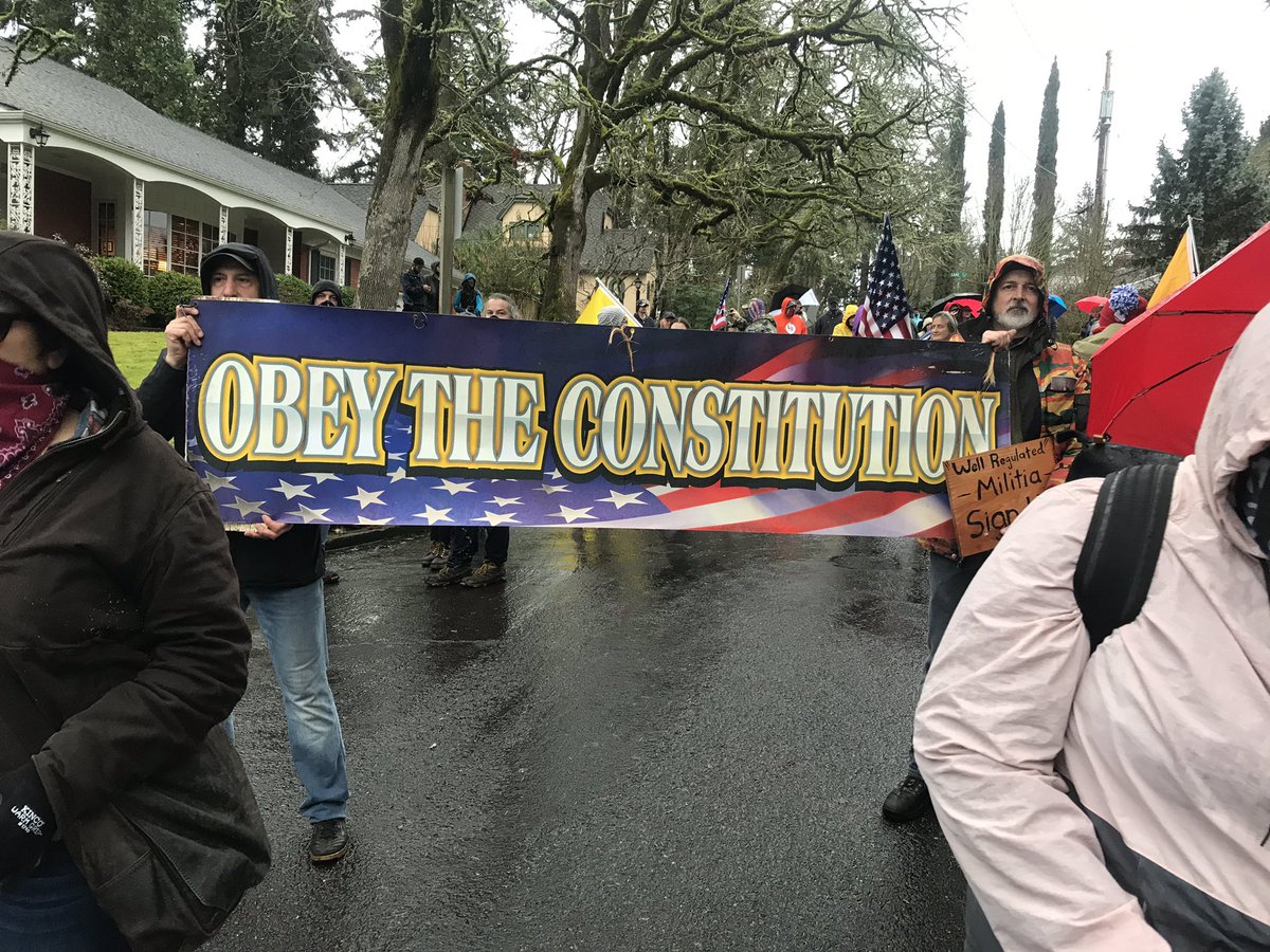 Man hold signs reading “Kate Brown dictator clown”