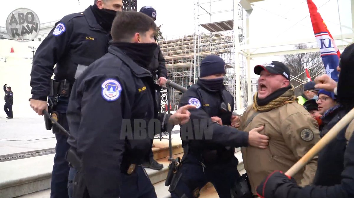One rioter in a tan coat with a US Marine Corps patch on the left sleeve attacks an officer.