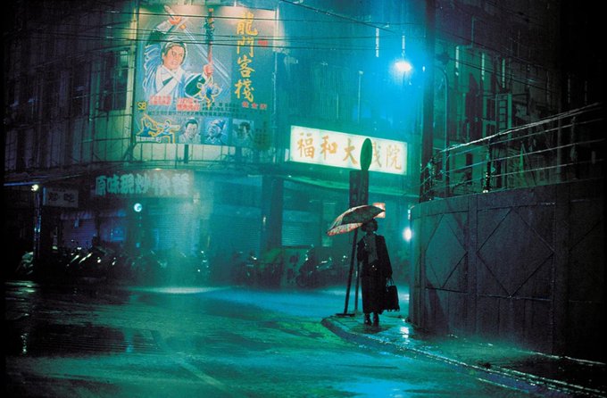 Long shot of Shiang-chyi Chen standing in the rain with an umbrella in Tsai Ming-liang's Goodbye Dragon Inn, cinema in the rain