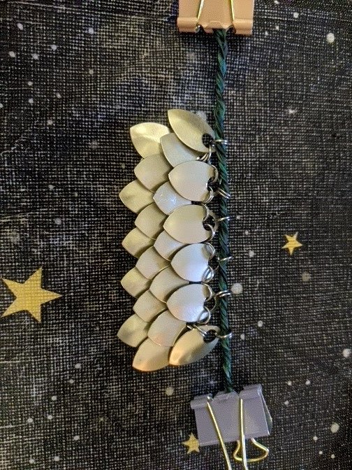 4 rows of the front side of small scalemail weaved together, champigne color on a black night sky tablecloth.