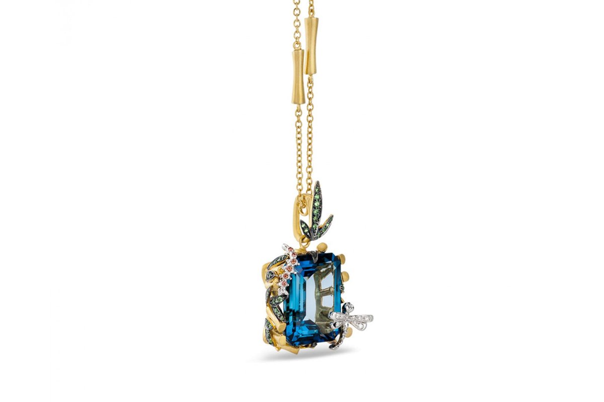 A garden on a pendant. Leaves (possibly weed), a dragon fly, maybe a caterpillar? around a pool of blue topaz.