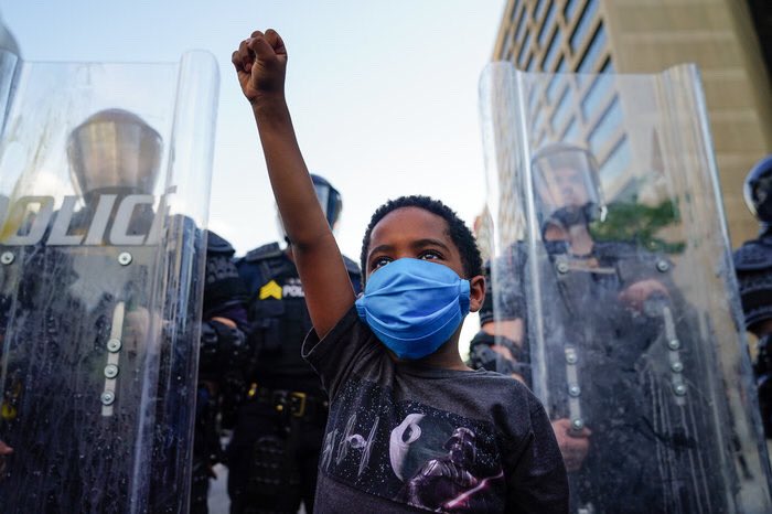 Photo of young boy protesting for Black Lives Matter in front of police.