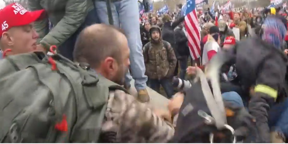 JakeGodin's tweet image. Images of the guy who was being super aggressive toward the journalist (there's something written on his hat "---ztown"?) and the one who assisted in pushing him over the stone railing (wearing camo with a backpack).