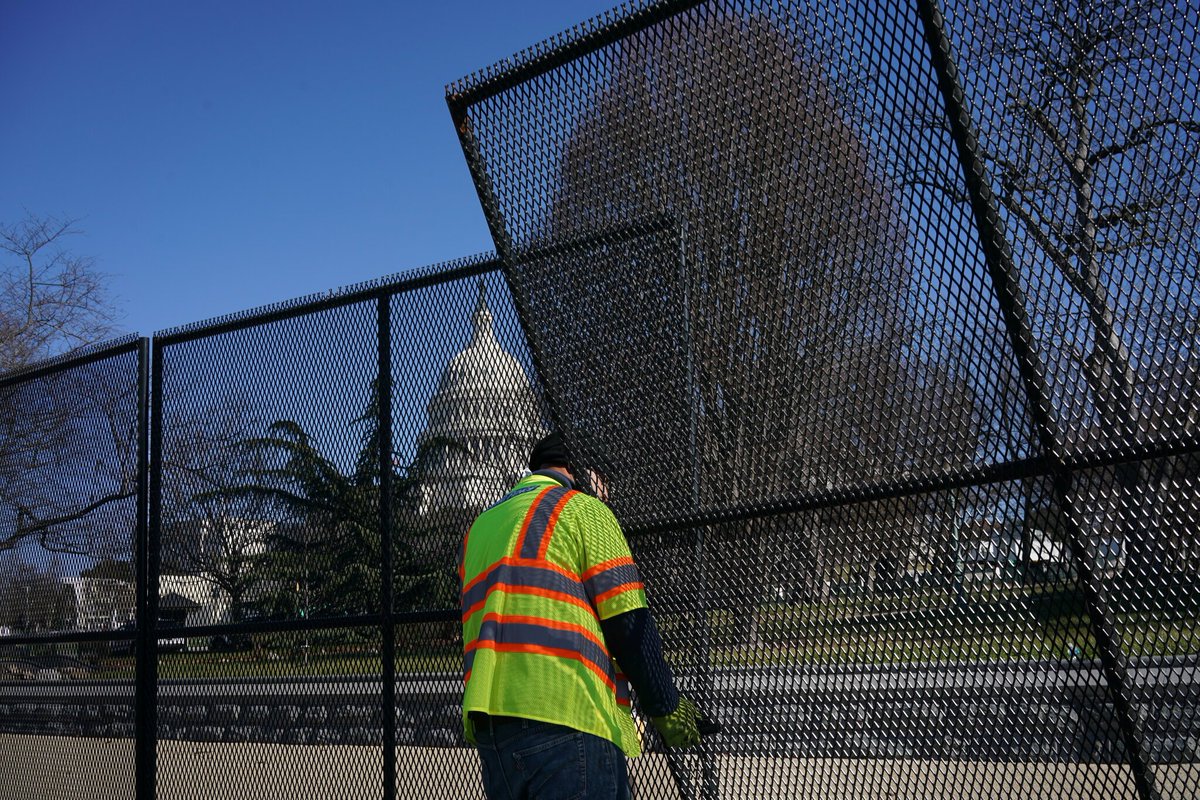 Closeup of a fence piece being installed by a worker. The Capitol building is in the background.