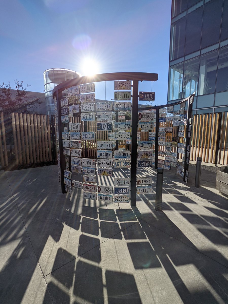 Picture of a sculpture with a bunch of license plates with the sun shining in the background