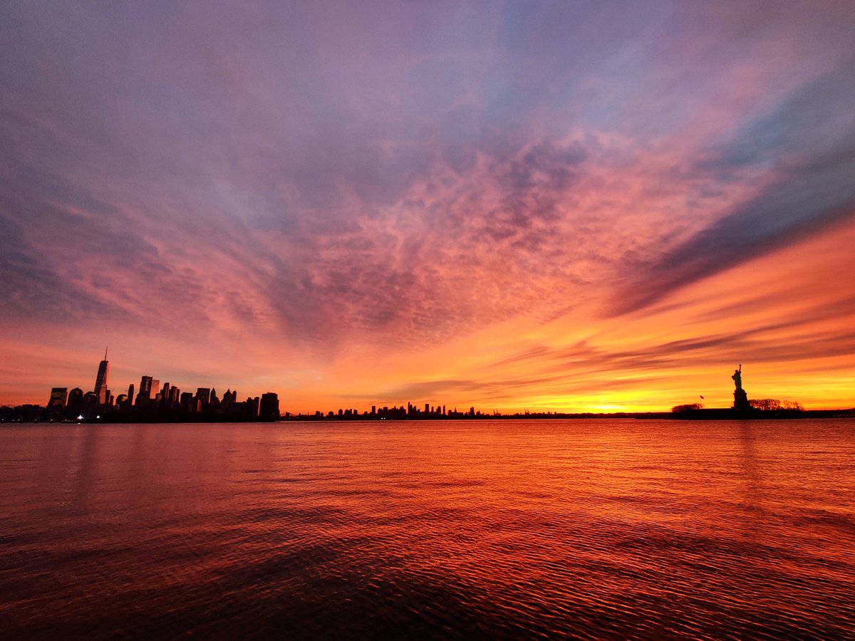 GaryHershorn's tweet photo. A beautiful way to start the week as the sun rises behind lower Manhattan, Brooklyn and the Statue of Liberty in New York City, Monday morning #newyorkcity #nyc #newyork @statueellisnps #sunrise @agreatbigcity https://t.co/mGu2FJdOzN
