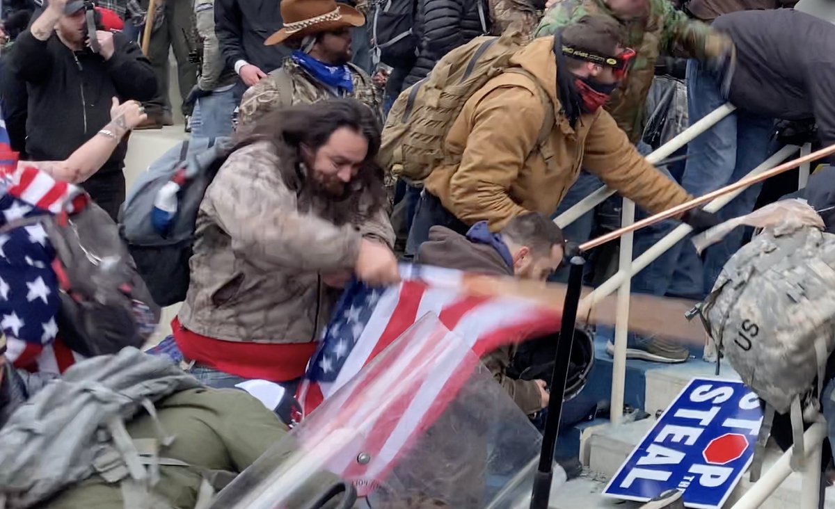 This "person of interest" is the man shown clearly in this screengrab, dressed in woodland camouflage, who beats a fallen officer at the inauguration door with an American flag.